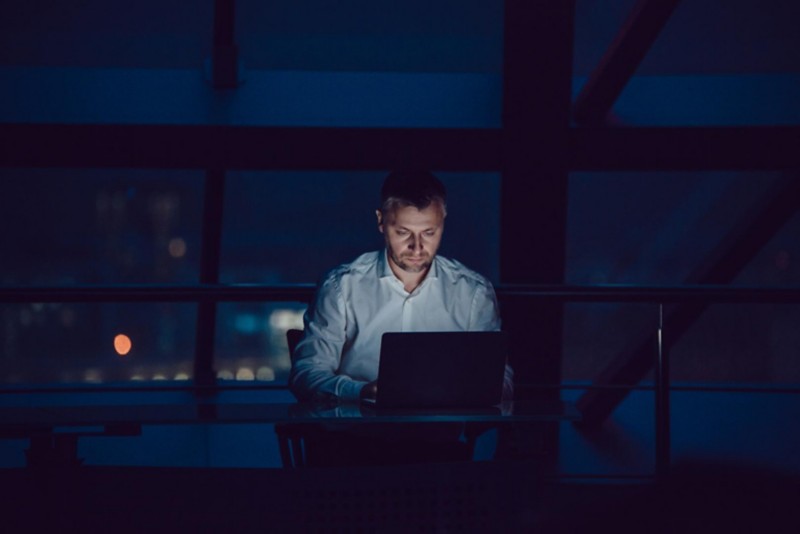 Mann sitzt bei Dunkelheit im Büro und arbeitet an einem Computer