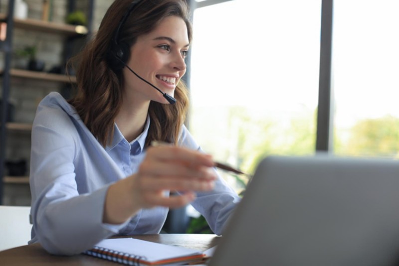 Frau mit Bluetooth Headset vor dem Laptop im Home Office